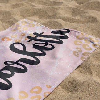 Close up of a personalized beach towel with leopard print pattern resting on beach sand on a sunny summer day.