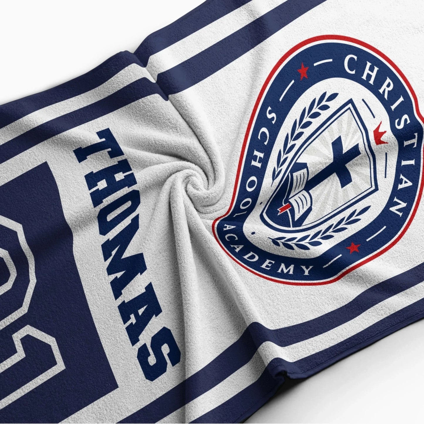 Close up of a soft personalized beach towel showing the Christian School Academy logo and the custom name Thomas.