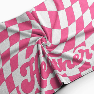 Close up of a plush pink and white wavy checkerboard beach towel with the custom name Heather in retro lettering.