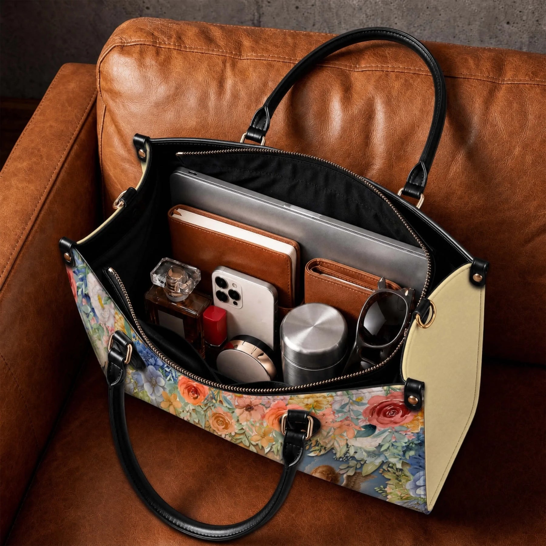Interior view of a floral handbag filled with daily essentials like a laptop, phone, perfume, and water bottle.