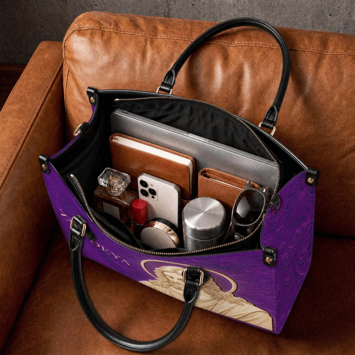 Spacious interior of a religious print purple leather handbag holding a laptop notebook and daily accessories.