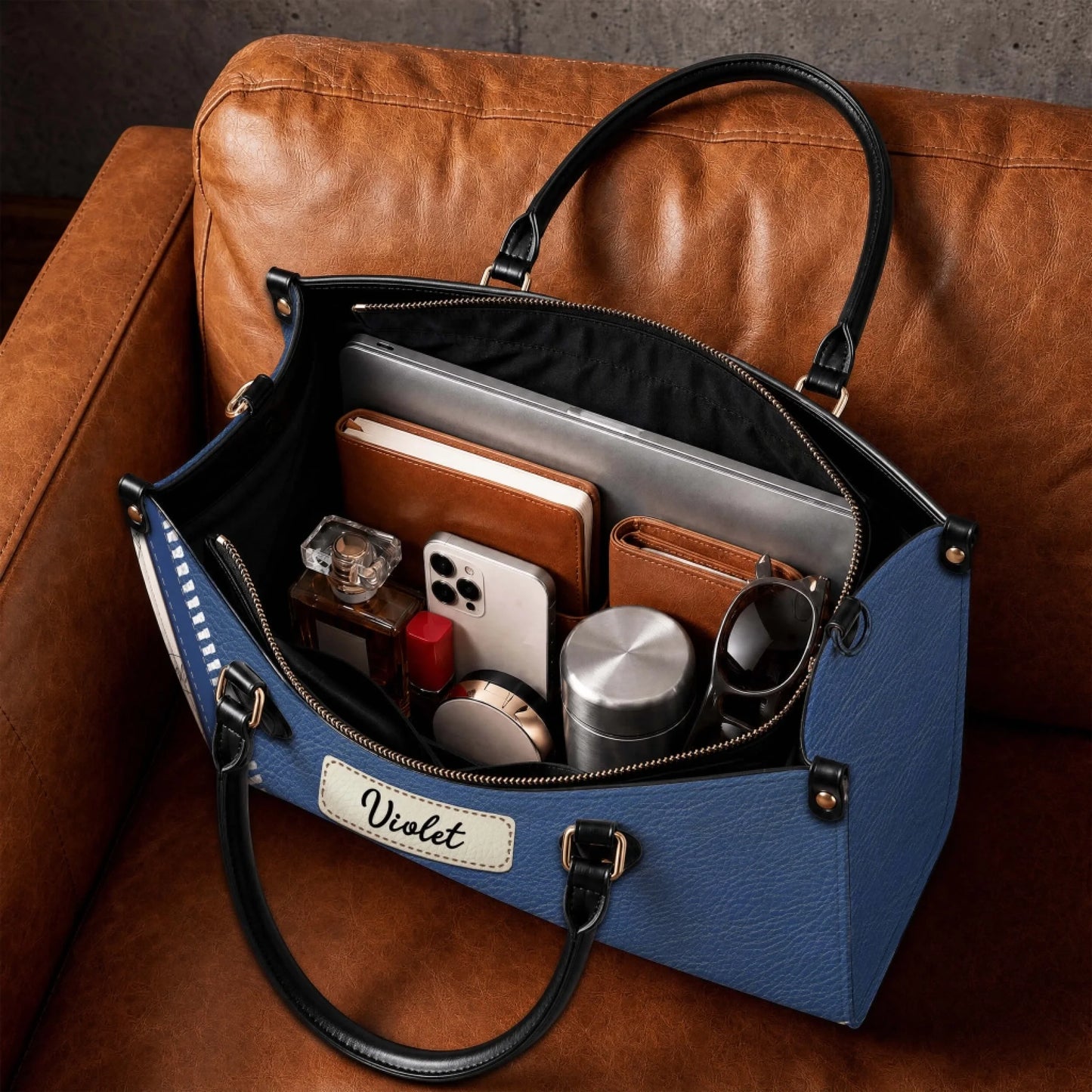 Inside view of a large personalized nurse handbag filled with daily essentials, laptop, and notebook on a leather sofa.