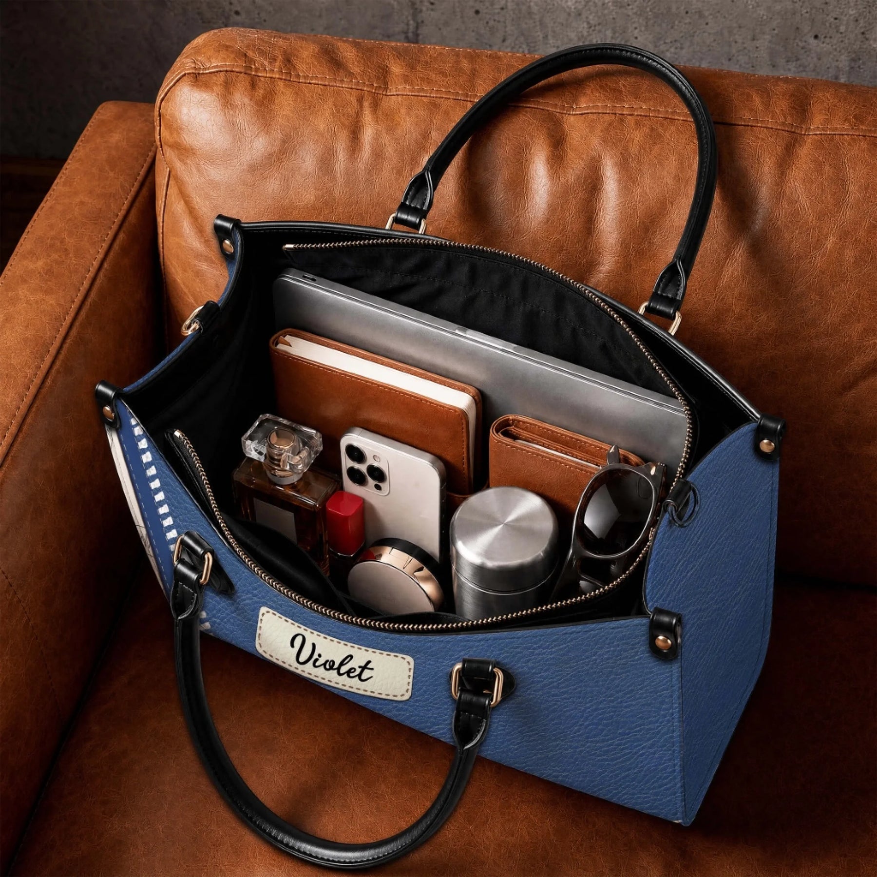 Inside view of a large personalized nurse handbag filled with daily essentials, laptop, and notebook on a leather sofa.