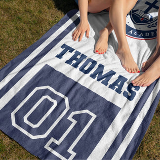 A student beach towel with the Christian School Academy emblem, customized with the name Thomas and number 01.
