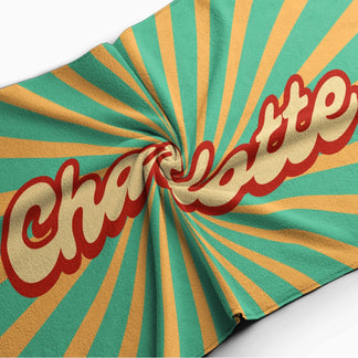 A spiraled beach towel showcasing a custom Charlotte design in a retro sunburst style with vibrant color tones.
