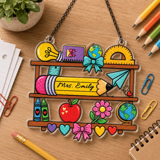 Personalized Mrs. Emily teacher school-themed ornament sitting on a desk with pencils, paper, and paperclips.