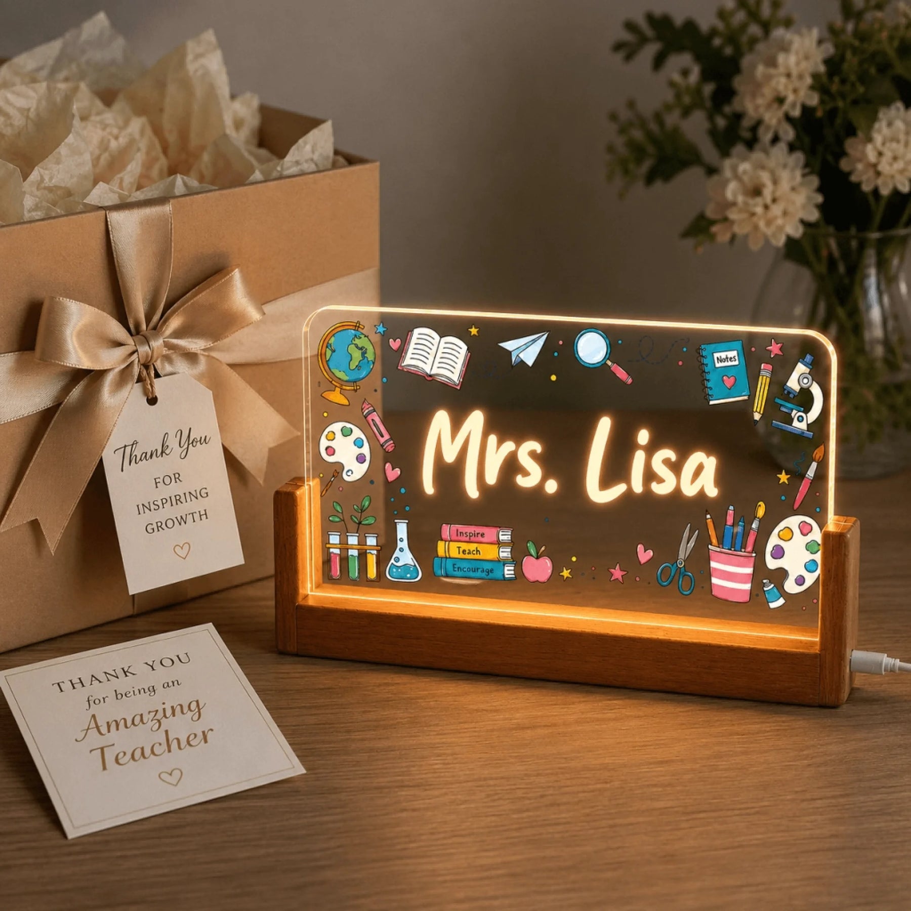 An illuminated personalized acrylic plaque for a teacher, featuring 'Mrs. Lisa', next to a gift box with a 'Thank You' tag and a greeting card.
