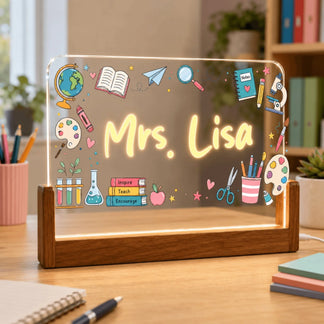 A personalized glowing acrylic plaque displaying 'Mrs. Lisa' and school-themed graphics, resting on a wooden base in a bright room setting.