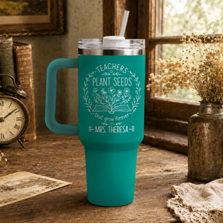 Teal personalized teacher tumbler with Teachers Plant Seeds graphic displayed on a wooden desk with antique books.