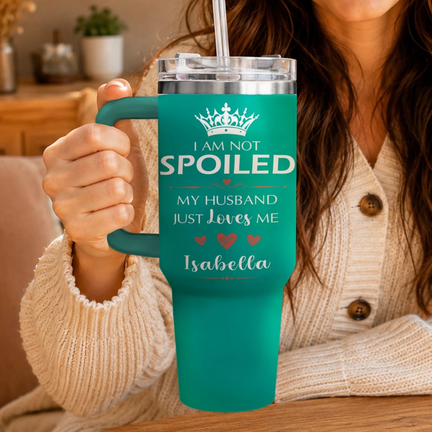A person holding a teal travel tumbler featuring personalized I am not spoiled text.