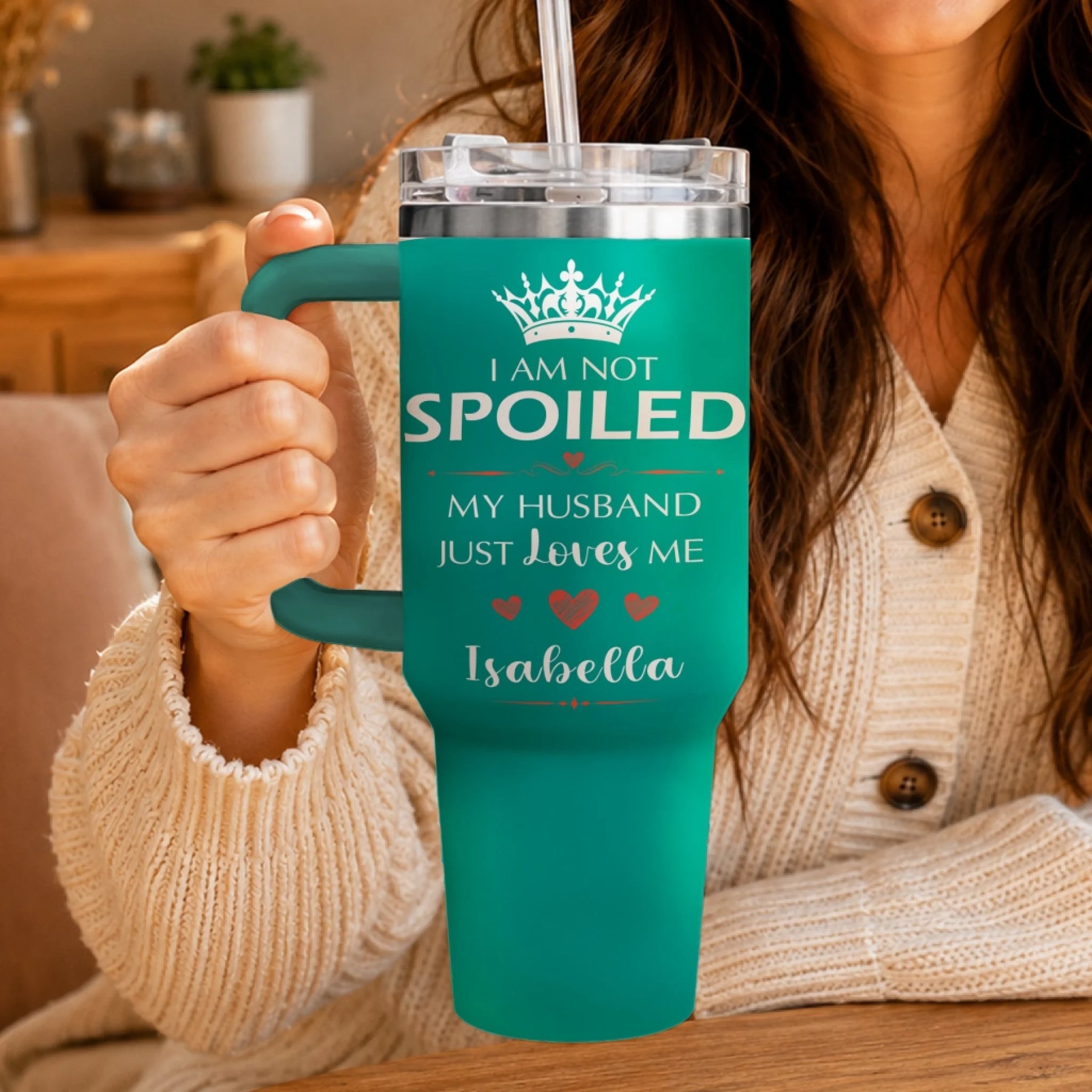 A person holding a teal travel tumbler featuring personalized I am not spoiled text.