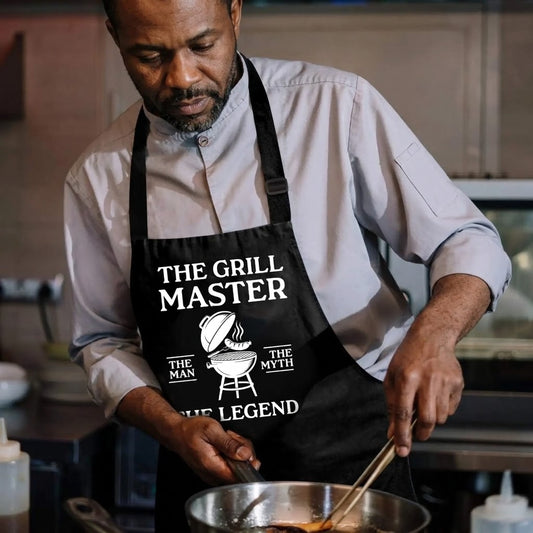 A man wearing a black grill master apron featuring a barbecue grill illustration and The Man The Myth The Legend text.