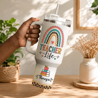 Hand holding a personalized teacher life tumbler with a rainbow stack of books and the custom name Theresa.