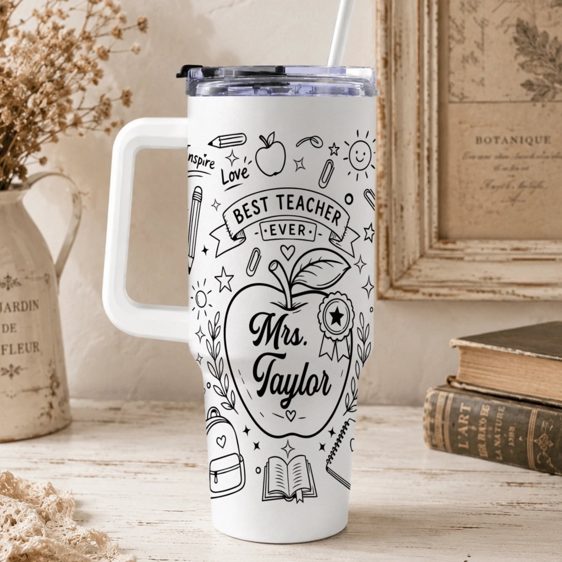 A white insulated tumbler for teachers, featuring black drawings of pencils, books, and an apple with custom name text.