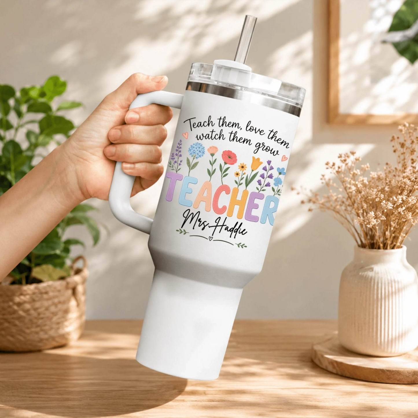Hand holding a white stainless steel teacher tumbler with a lid and straw, featuring a colorful floral bouquet design.