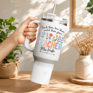 Hand holding a white stainless steel teacher tumbler with a lid and straw, featuring a colorful floral bouquet design.