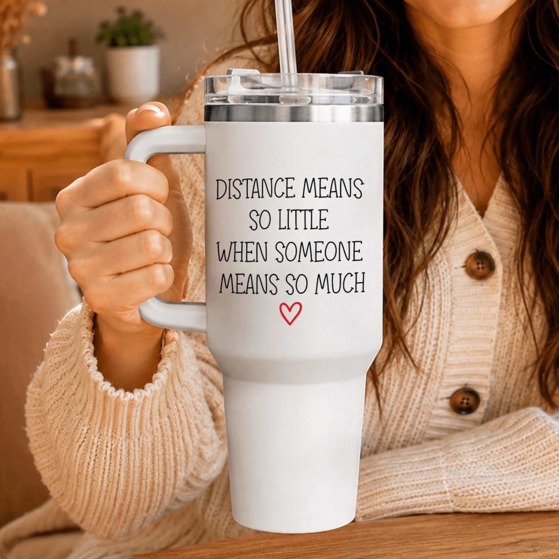 Person holding a personalized white tumbler with handle featuring the long distance relationship quote and red heart icon.