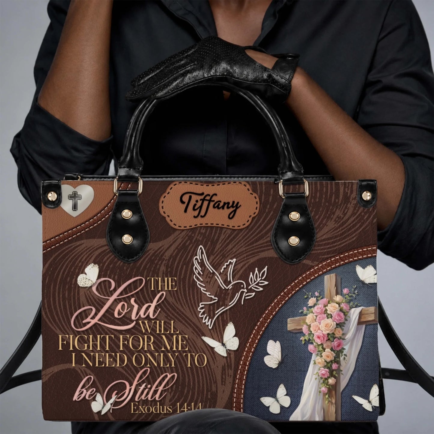 A woman wearing black gloves holding a personalized faith inspired tote bag with floral cross and butterfly designs.