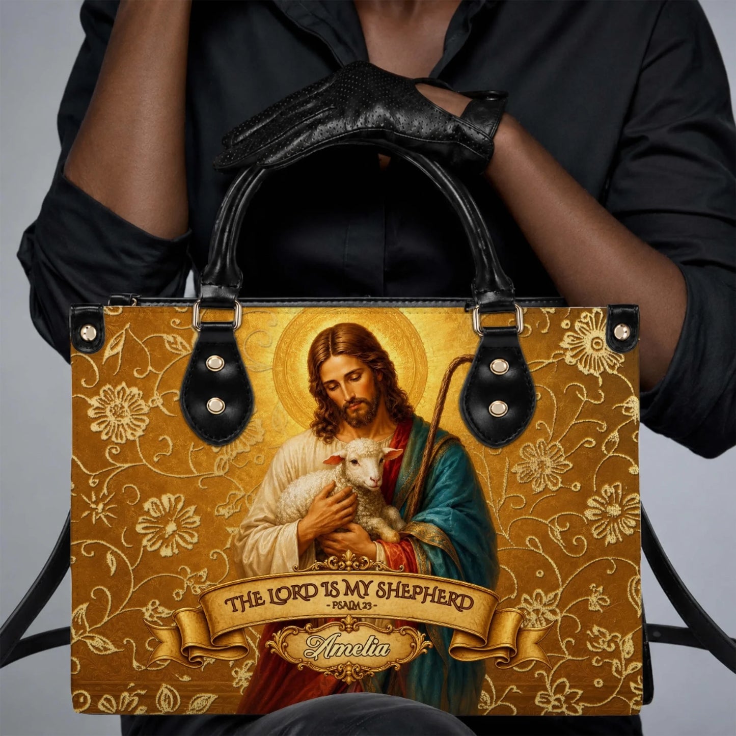 A woman wearing a black outfit holding a personalized Christian handbag featuring a gold floral design and Psalm 23.
