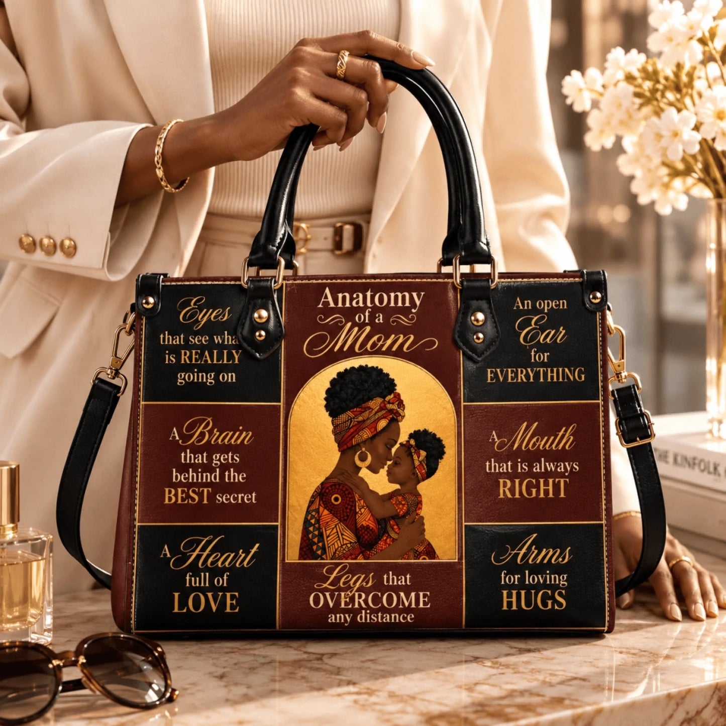 Close up of a woman holding an Anatomy of a Mom leather shoulder bag with inspirational text and artistic design.