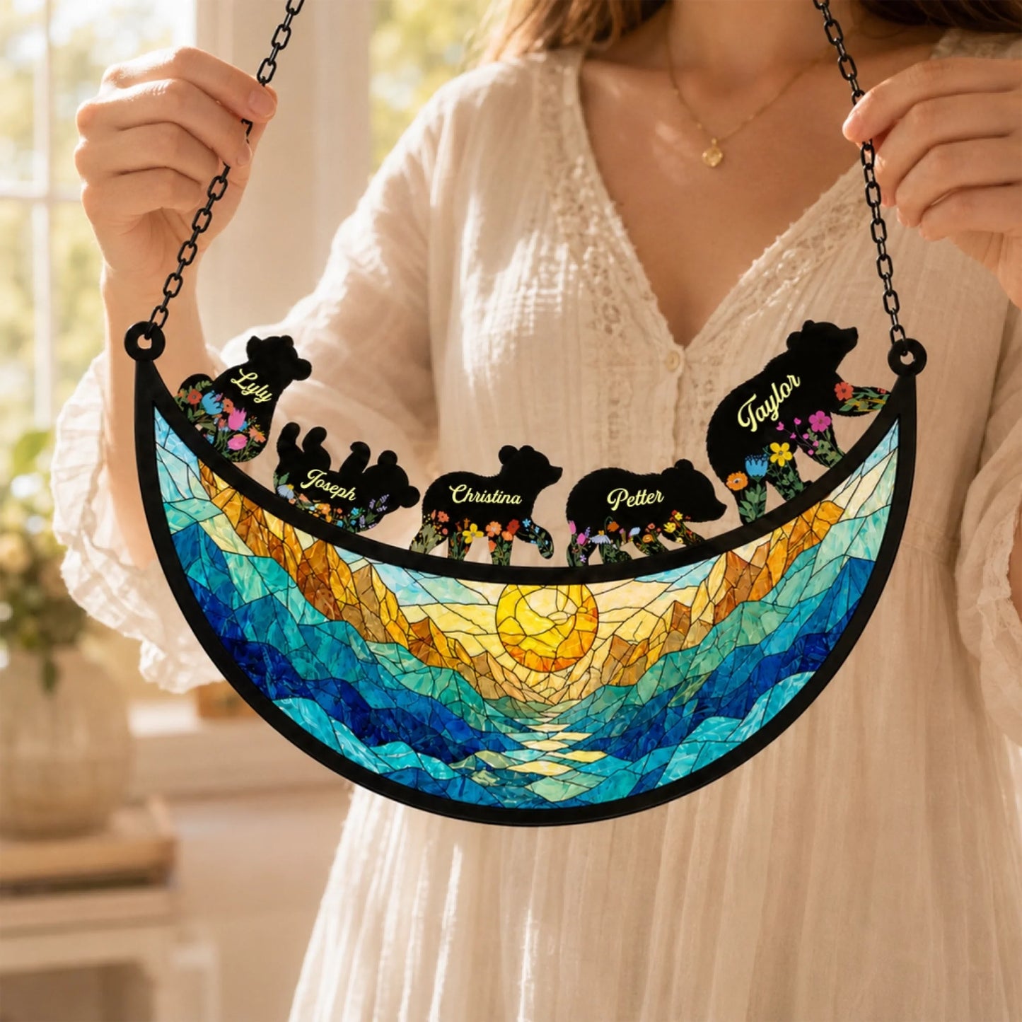 A woman holding a personalized family bear suncatcher gift with a beautiful mountain sun design and custom names.