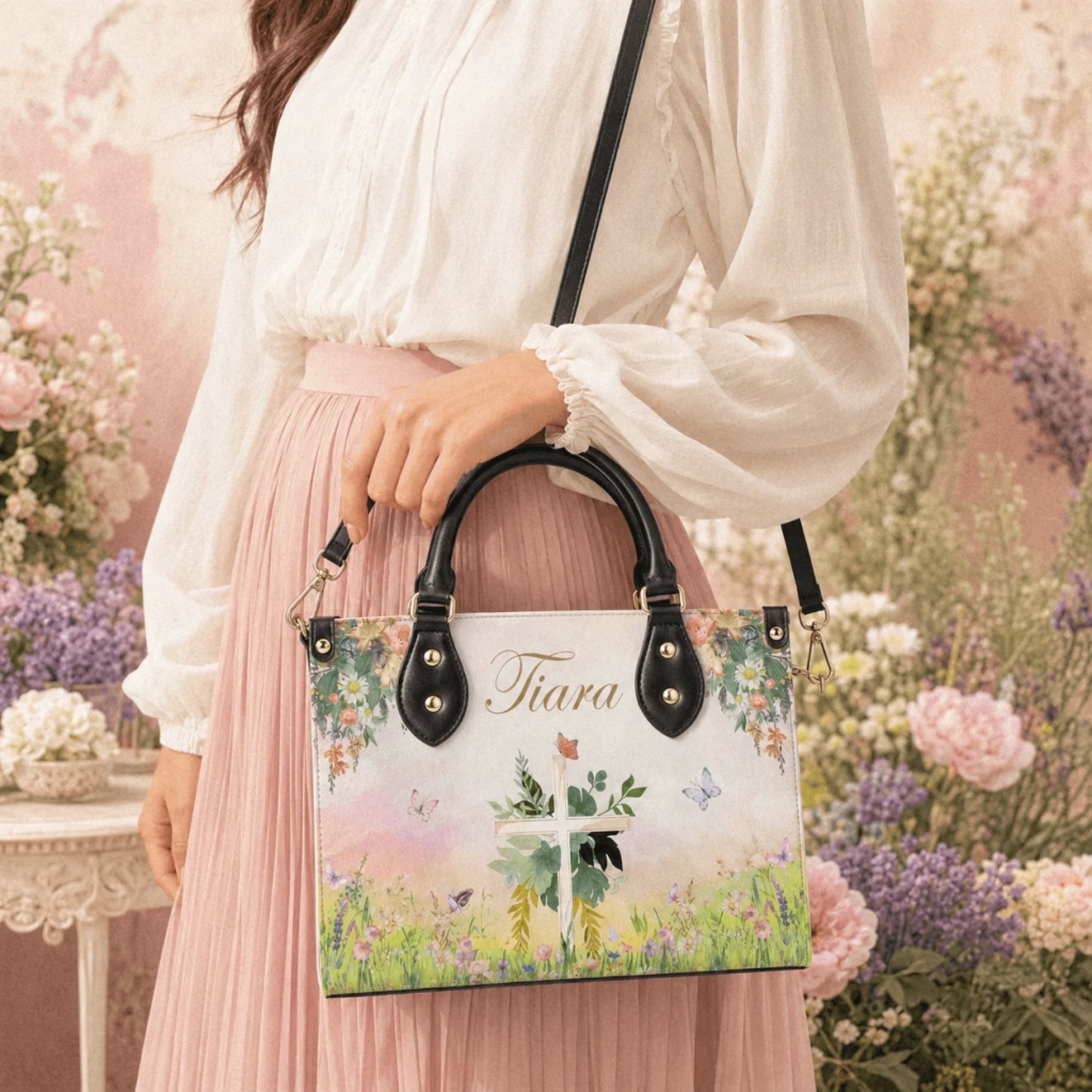 A woman holding a personalized PU leather handbag featuring a floral cross design and the custom name Tiara in a garden setting.