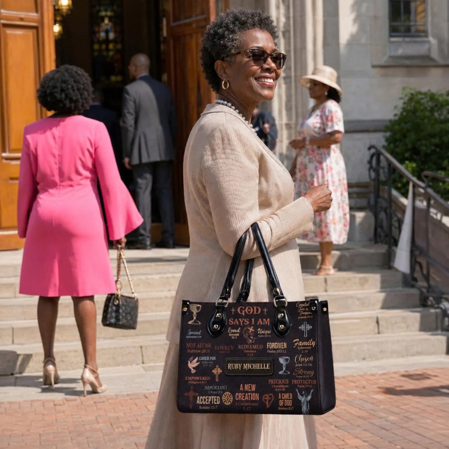 A woman wearing a beige suit holds a personalized Ruby Michelle handbag with faith based scripture verses outside church.