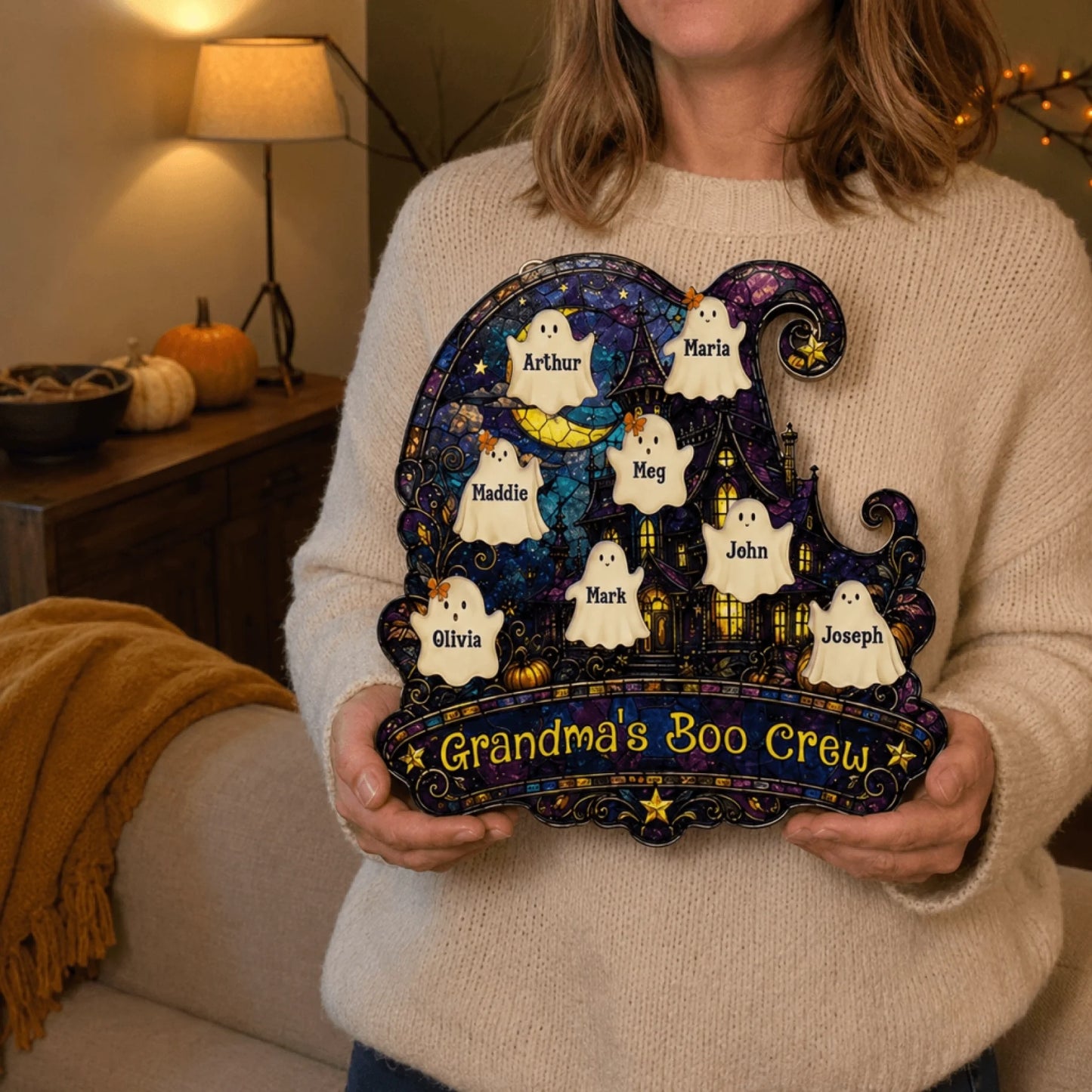 A woman holding a custom Grandma's Boo Crew acrylic wall hanging decorated with cute ghosts and family names.