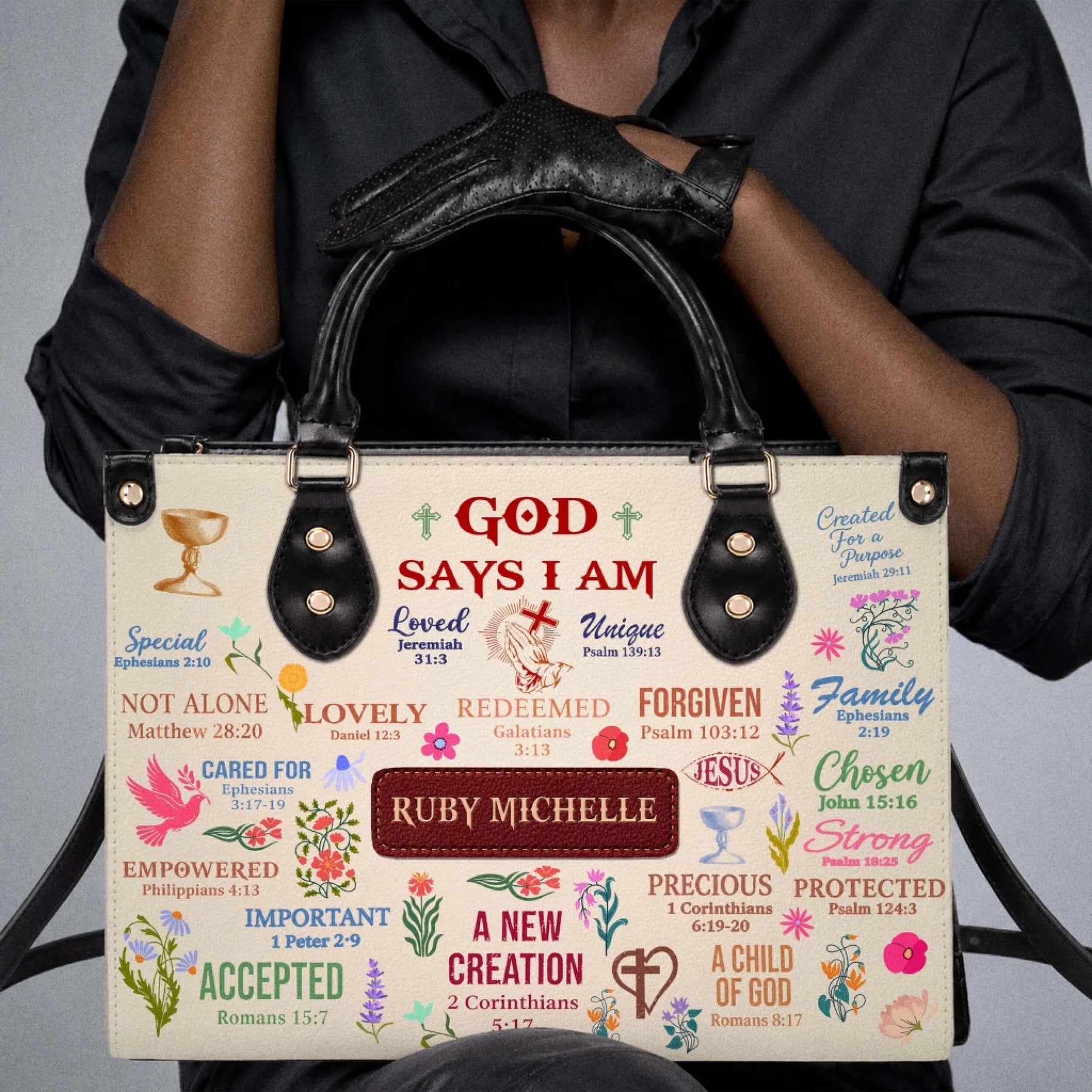 Person holding a custom-named religious handbag decorated with spiritual quotes and colorful floral illustrations.