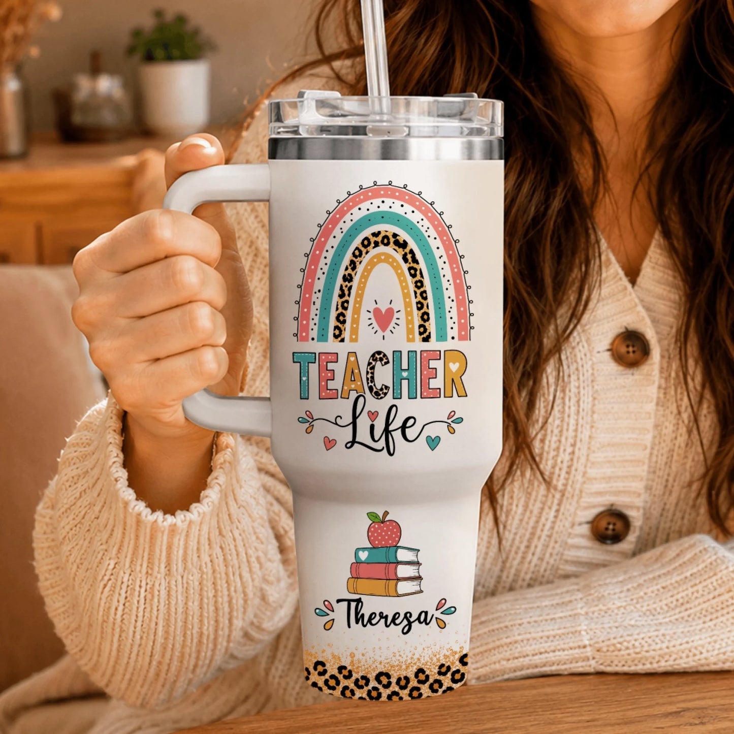 Woman in a beige cardigan holding a custom white teacher life tumbler with rainbow and leopard print details.