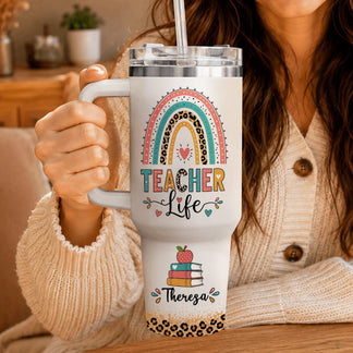 Woman in a beige cardigan holding a custom white teacher life tumbler with rainbow and leopard print details.