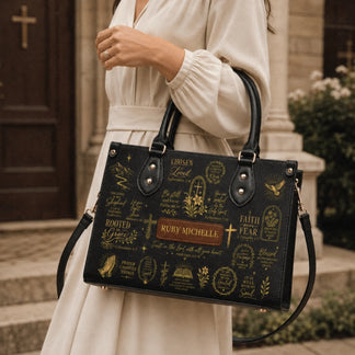 Close up of a woman holding a black custom handbag printed with scripture verses and floral religious gold art.