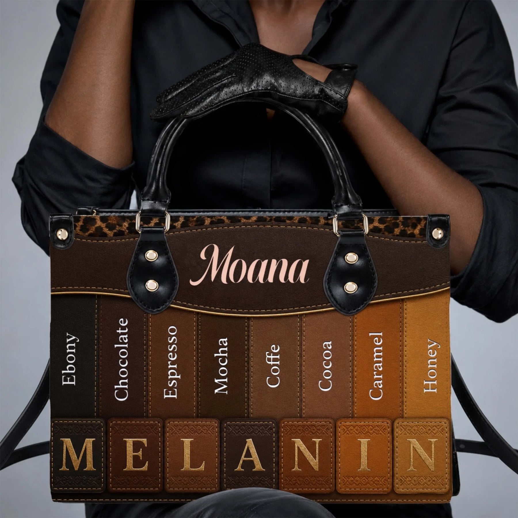 Close up of a woman wearing black gloves holding a personalized melanin-themed handbag with varied skin tone shades.