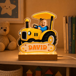 Light-up acrylic tractor lamp with baby photo and custom name David, placed on a nursery bookshelf.