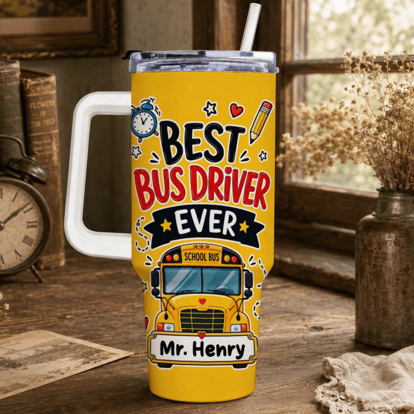 A yellow tumbler with a white handle and straw, displaying "BEST BUS DRIVER EVER", a school bus graphic, and "Mr. Henry" by a window.
